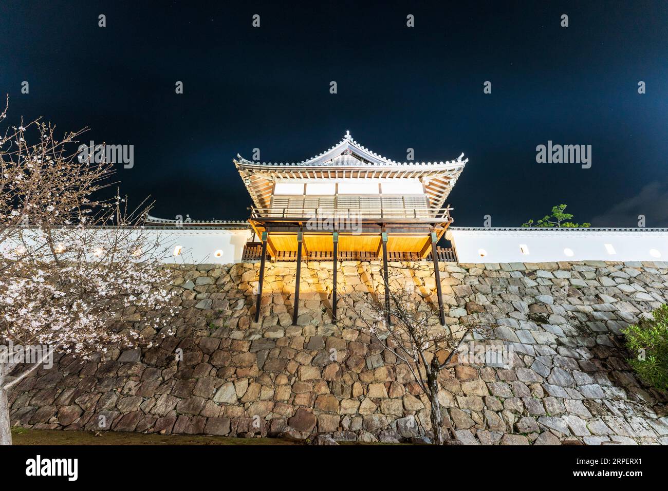 Yudono Badehaus in Fukuyama Burg hoch auf der Honmaru Vorhangsteinmauer. Blick aus einem niedrigen Winkel auf das Holzgebäude, das nachts beleuchtet wird. Stockfoto