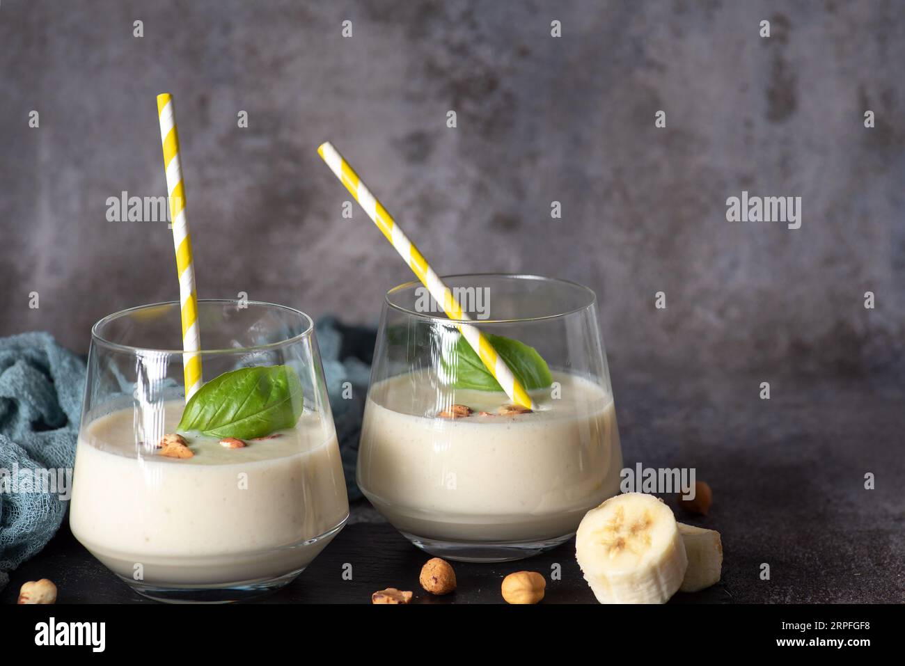 Frischer, gesunder Smoothie mit Banane und Haselnüssen, in einem Glasbecher mit gelb-weißem Trinkschlauch Stockfoto