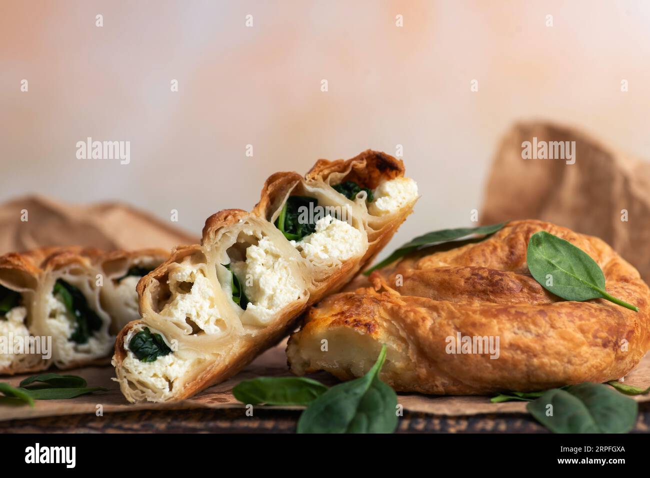Hausgemachte, frisch gebackene, rohe Spinatkuchen auf Backpapier, dekoriert mit frischen Spinatblättern, auf hellem Hintergrund Stockfoto