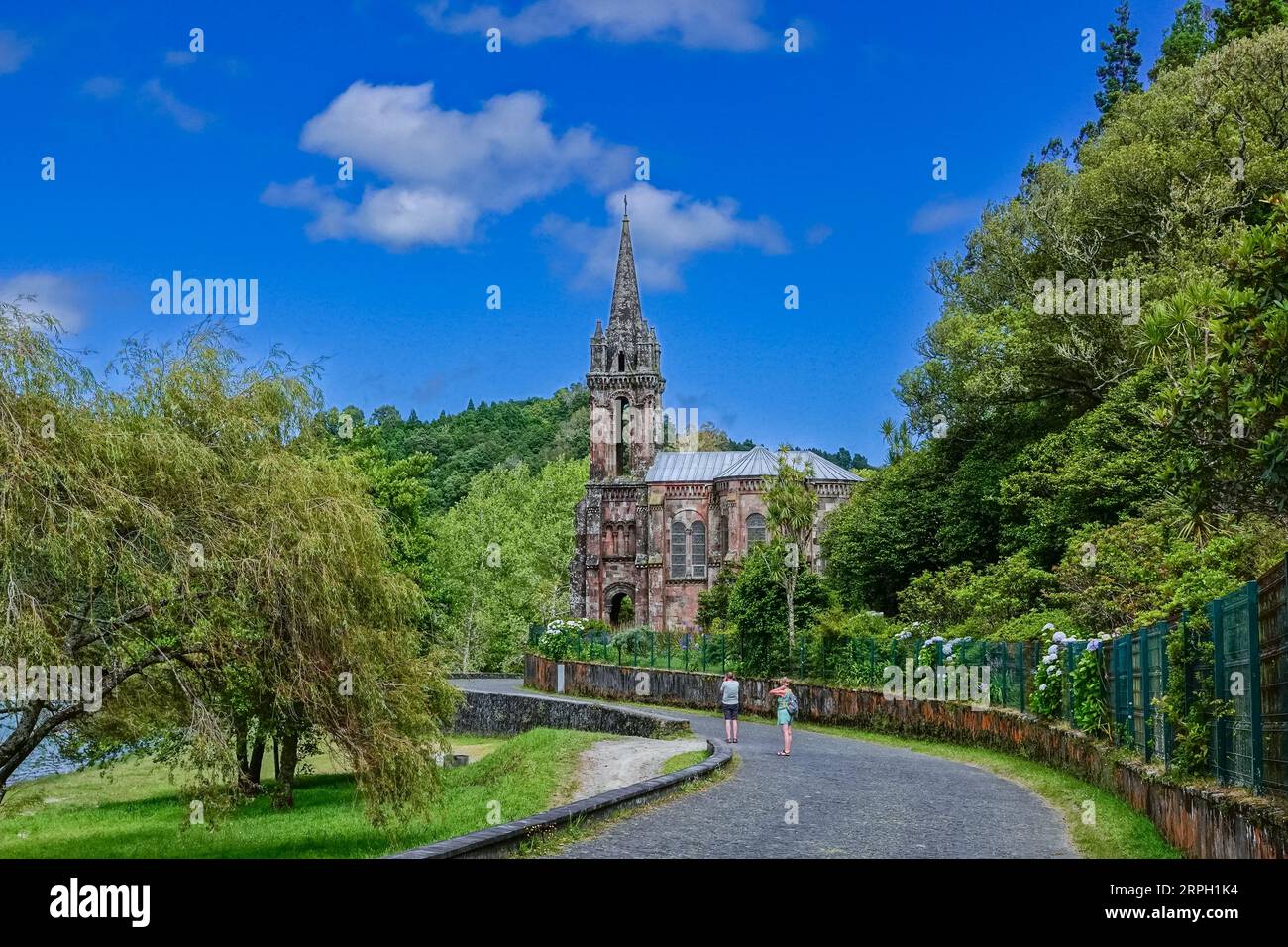 Ein Paar spaziert vorbei an der privaten Kapelle der Capela de Nossa Senhora das Vitórias am Furnas-See auf der Azoren-Insel Sao Miguel in Furnãs, Portugal. Stockfoto