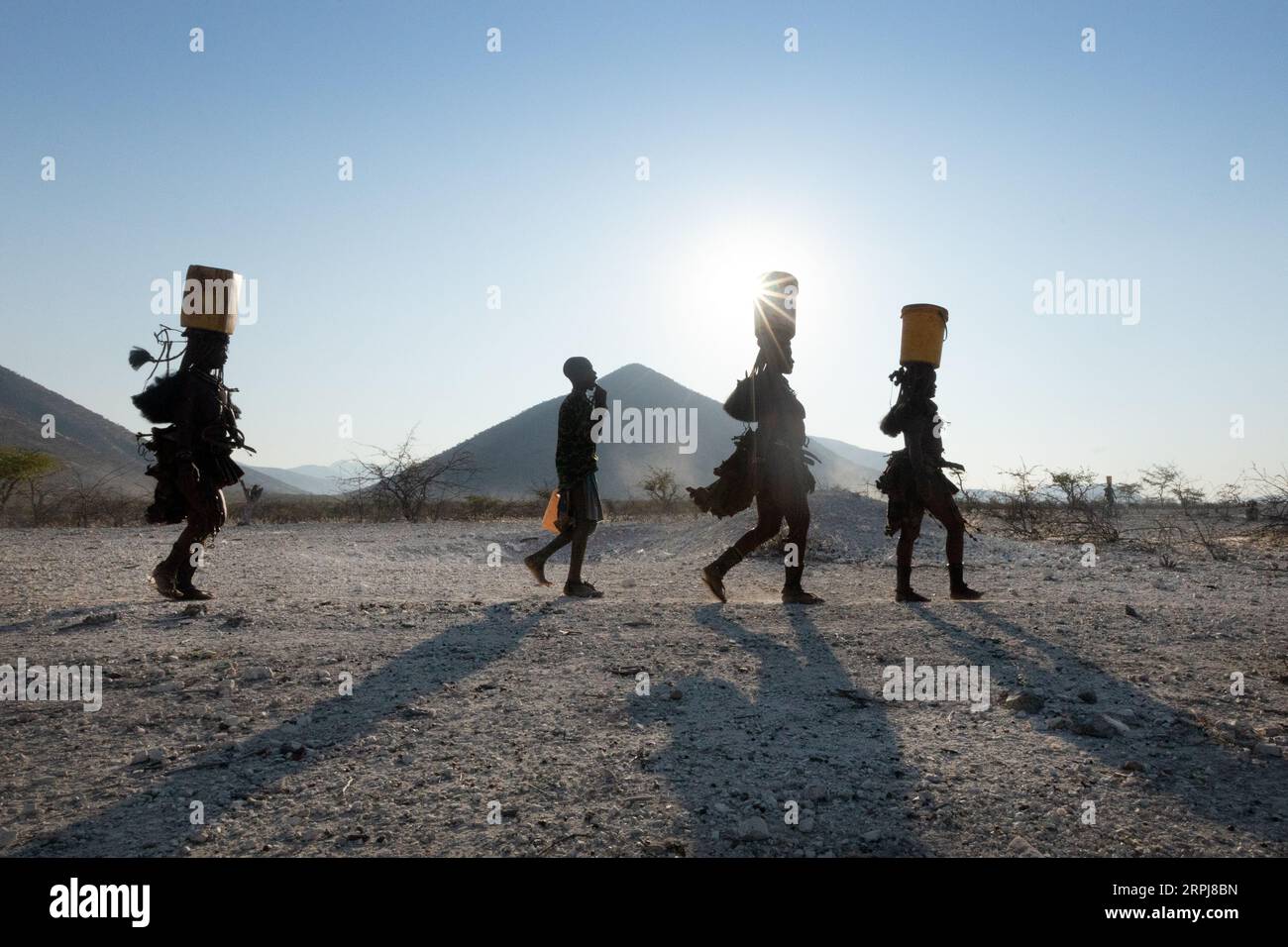 Himba-Frauen laufen alle in einer einzigen Linie, während sie von der Wassersammlung zurückkehren. Wasser ist im Norden Namibias erschreckend, daher müssen alle Rationen gesammelt werden Stockfoto