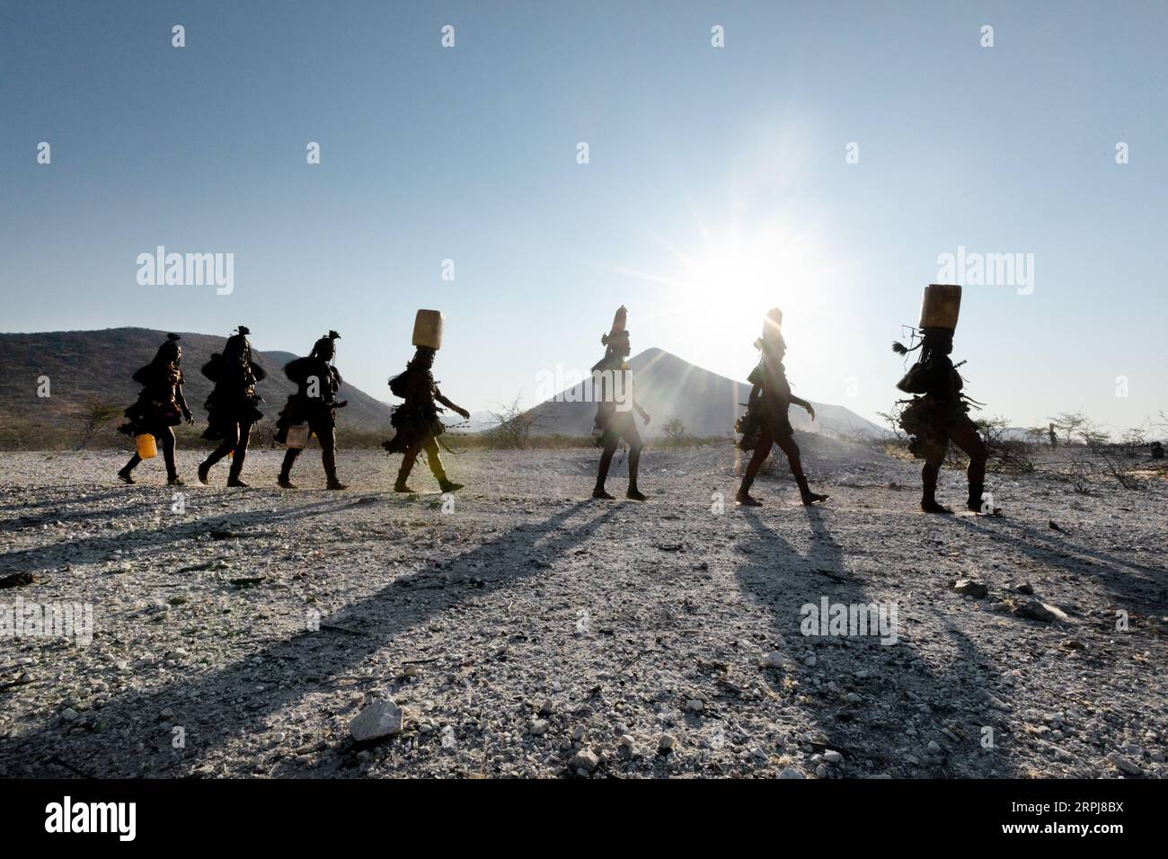 Himba-Frauen laufen alle in einer einzigen Linie, während sie von der Wassersammlung zurückkehren. Wasser ist im Norden Namibias erschreckend, daher müssen alle Rationen gesammelt werden Stockfoto