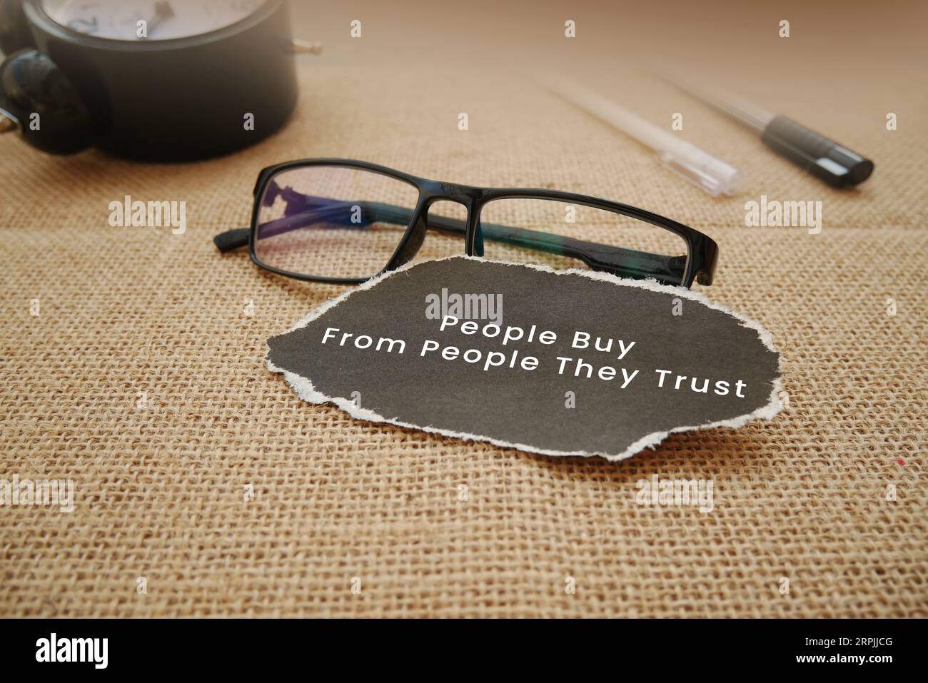 Eine Wecker, Gläser, Stift und ein zerrissenes Stück Cremepapier, das mit Menschen geschrieben wurde, kaufen von Menschen, denen sie vertrauen, auf hölzernem Hintergrund Stockfoto