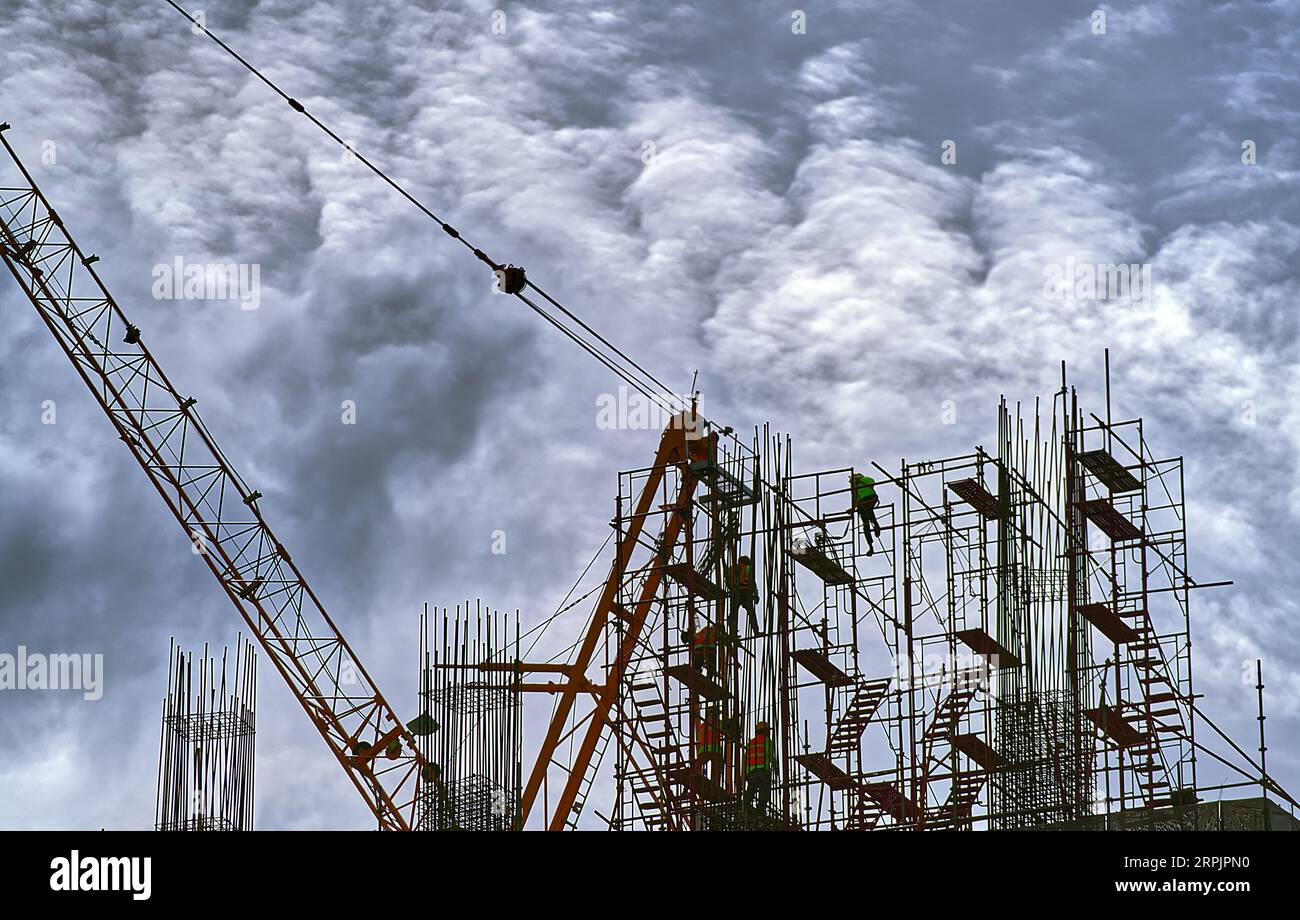 Landschaftsbild von Arbeitern, die auf einer Baustelle auf der Oberseite eines Gebäudes arbeiten, massive Wolken Himmel Hintergrund. Stockfoto