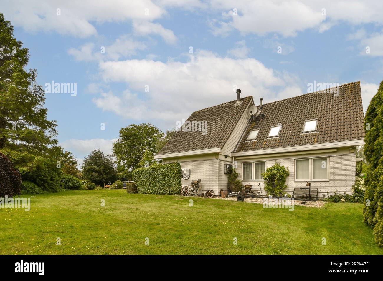 Ein kleines Haus in der Mitte eines Grasgebietes mit Bäumen und Büschen auf beiden Seiten des Hauses gibt es einen blauen Himmel Stockfoto