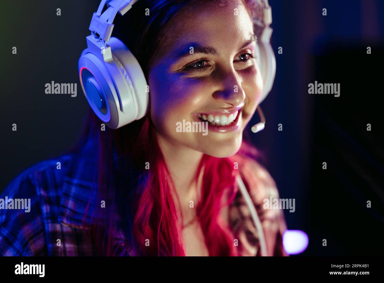 Weibliche Gamerin navigiert mit angeschalteten Kopfhörern durch ein Videospiel, streamt und teilt ihre Leidenschaft mit der Online-Gaming-Community. Mit einem Headset ist sie voll Stockfoto