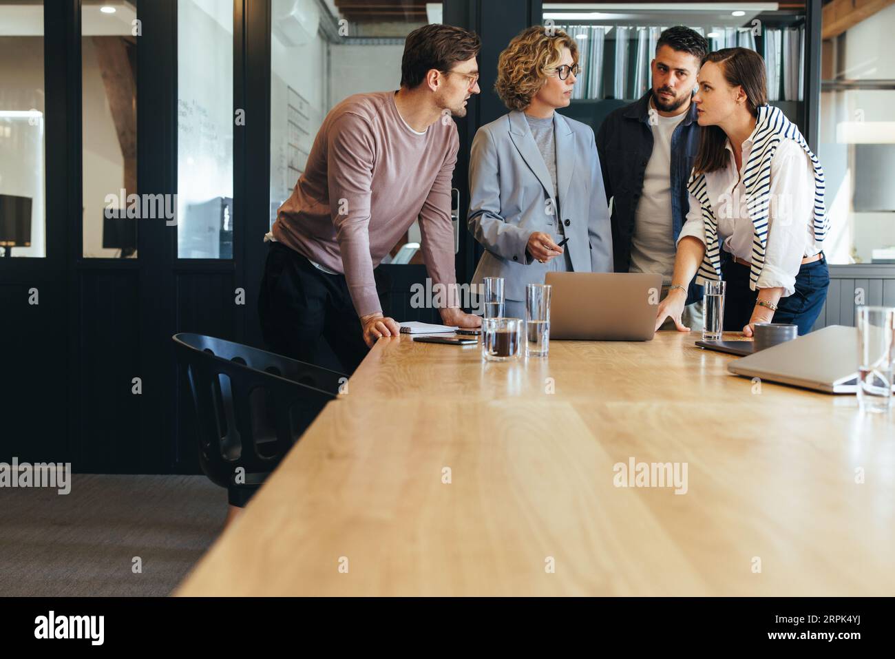 Designteam, das ein Projekt in einer Besprechung diskutiert, steht es in einem Sitzungssaal um einen Laptop herum. Gruppe von Geschäftsleuten, über die gesprochen wird Stockfoto