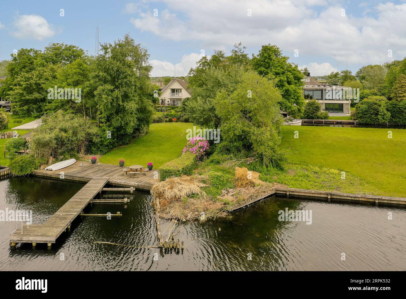 Eine Bootsanlegestelle in der Mitte eines Gewässers, umgeben von üppigen grünen Bäumen und Häusern auf beiden Seiten Stockfoto