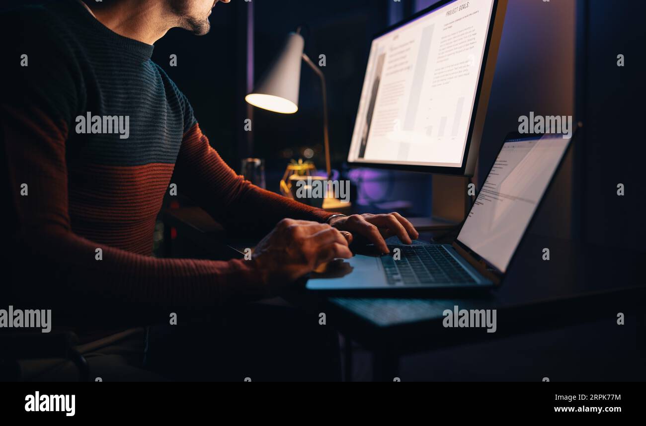 Ein kaukasischer männlicher Unternehmer arbeitet spät von seinem Heimatbüro aus und konzentriert sich auf ein Unternehmensprojekt. Er schreibt auf seinem Laptop, um eine Frist einzuhalten. Stockfoto