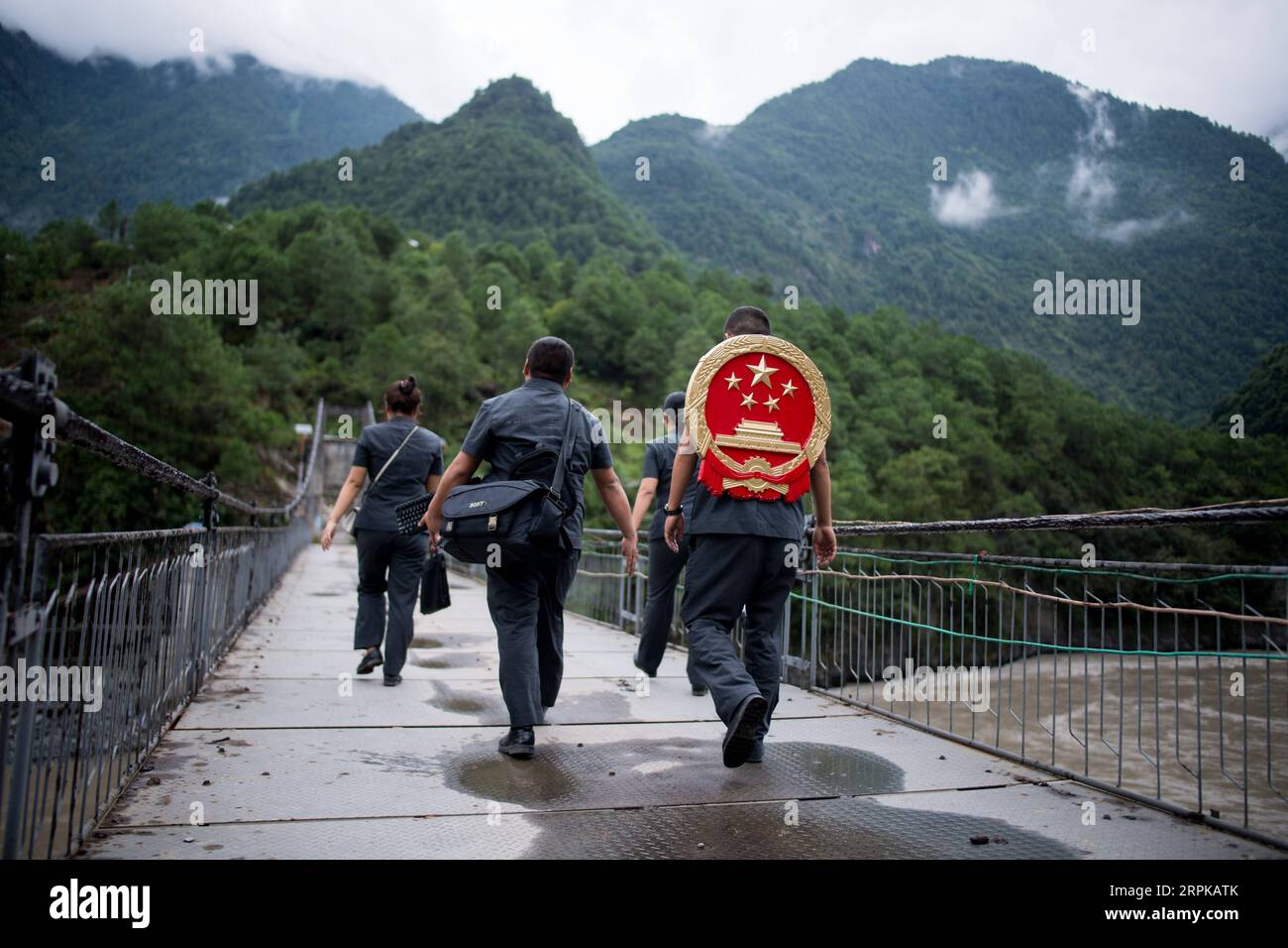 200105 -- PEKING, 5. Januar 2020 -- Deng Xing, Richter am Volksgericht des Gongshan County, trägt das nationale Emblem auf seinem Rücken, um mit seinen Kollegen auf einer Brücke über den Fluss Nujiang in der Autonomen Präfektur Nujiang Lisu, Provinz Yunnan im Südwesten Chinas, zu gehen. August 30, 2019. Aufgrund des unbequemen Transports in der gebirgigen Präfektur muss Deng oft das nationale Emblem auf dem Rücken zu Fuß tragen, um Anwohnern in ländlichen Gebieten Rechtsdienstleistungen zu erbringen. XINHUA-BILDER DES JAHRES 2019 JiangxWenyao PUBLICATIONxNOTxINxCHN Stockfoto