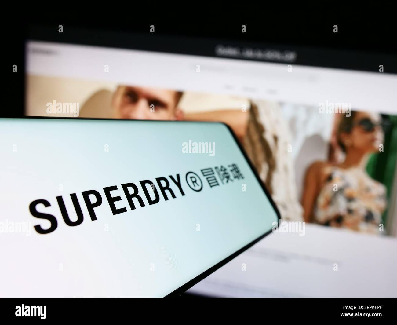 Smartphone mit Logo des britischen Bekleidungsunternehmens Superdry plc auf dem Bildschirm vor der Business-Website. Konzentrieren Sie sich auf die Mitte-links-Anzeige des Telefons. Stockfoto