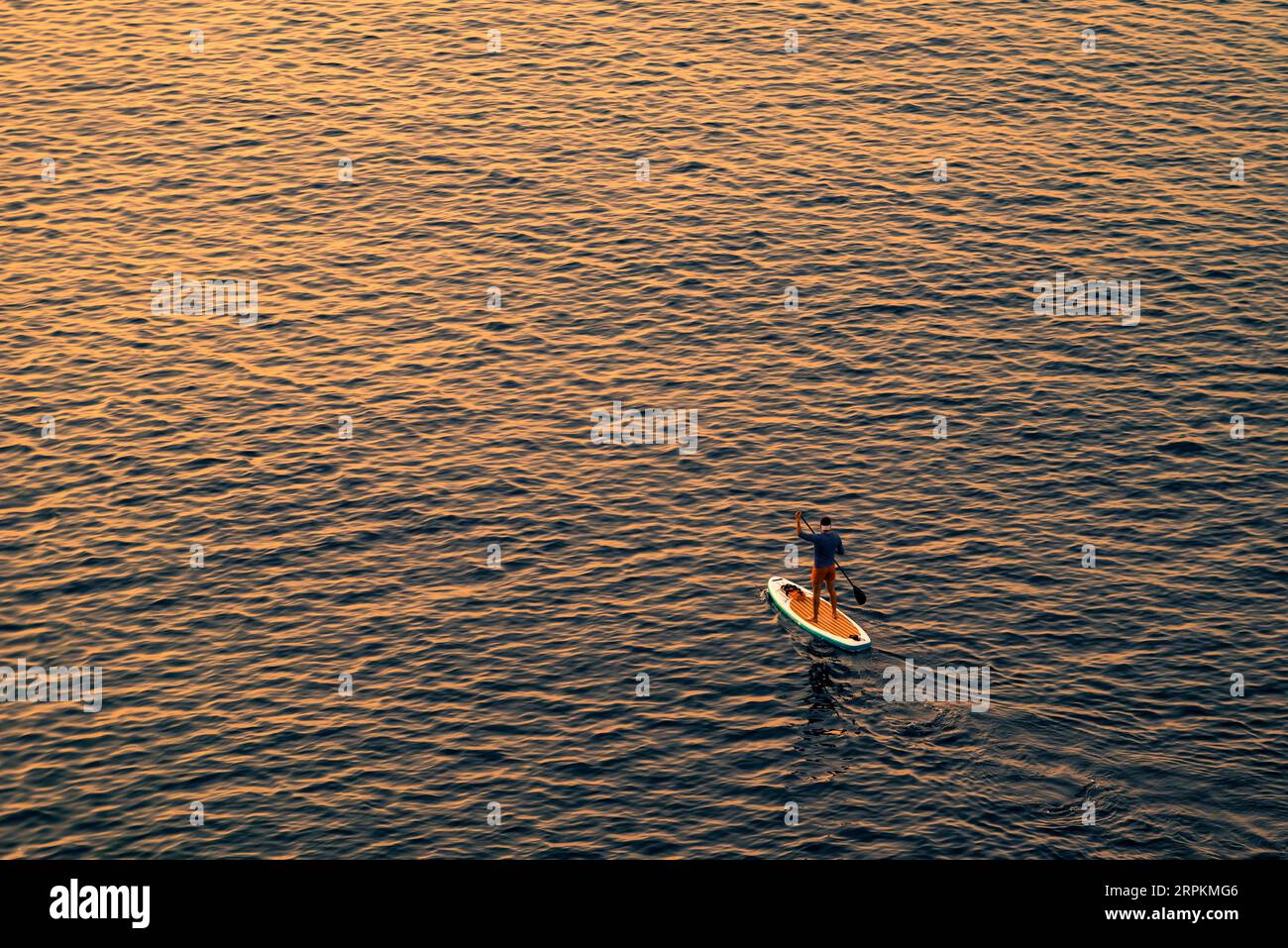 Abenteuerlustige Personen auf einem Stand-Up-Paddle-Board paddeln während eines hellen und lebendigen Sonnenaufgangs Stockfoto