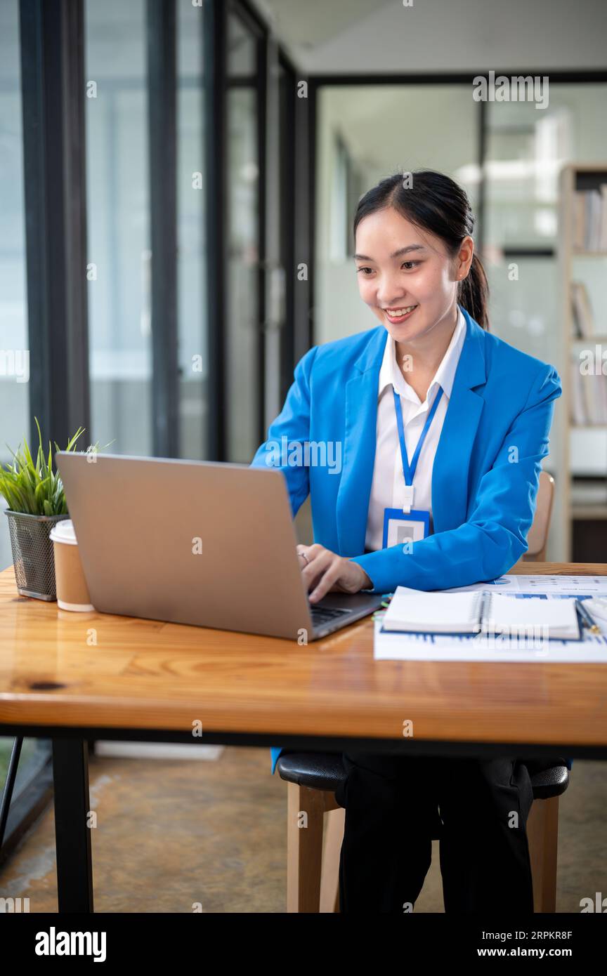 Eine professionelle und attraktive asiatische Geschäftsfrau oder Bankierin in einem blauen Business-Anzug arbeitet an ihrem Laptop Stockfoto