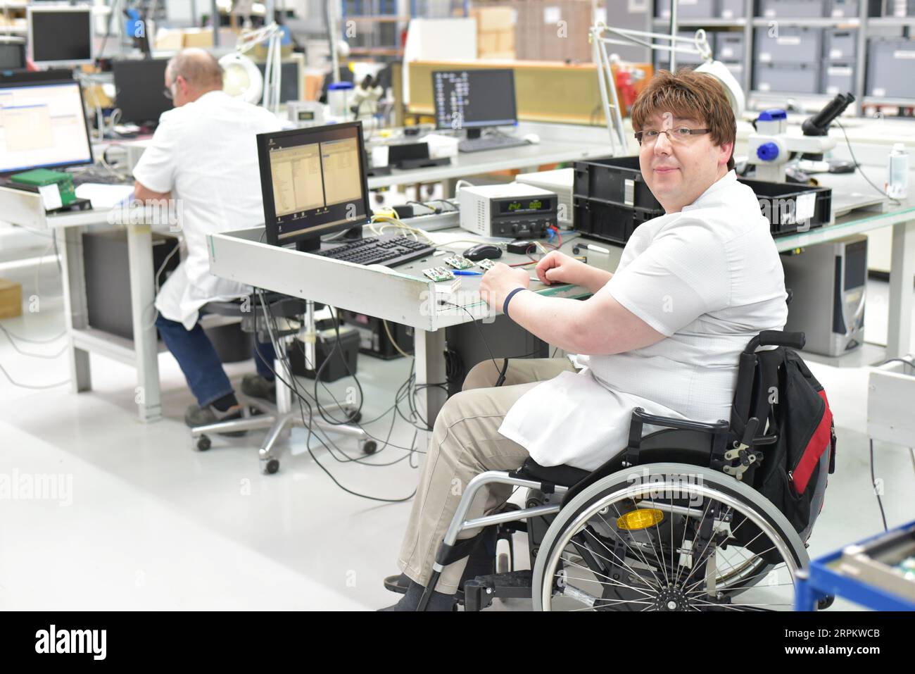 Behinderte im Rollstuhl an einem Arbeitsplatz in einer Elektronik-Fertigungs- und Montagefabrik Stockfoto