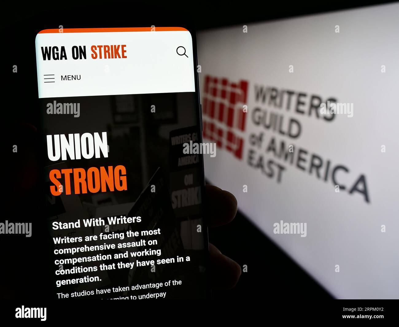 Person, die ein Smartphone mit einer Webseite der Labor union Writers Guild of America East (WGAE) auf dem Bildschirm mit Logo hält. Konzentrieren Sie sich auf die Mitte der Telefonanzeige. Stockfoto