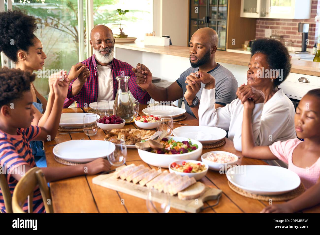 Die Familie Der Mehrgenerationen Ist Zu Hause Und Spricht Vor Dem Essen Ein Gebet Stockfoto