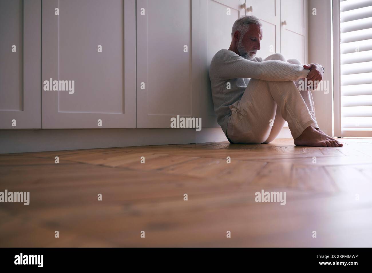 Depressiver Älterer Mann, Der Mit Schlechter Psychischer Gesundheit Leidet, Sitzt Zu Hause Auf Dem Boden Stockfoto