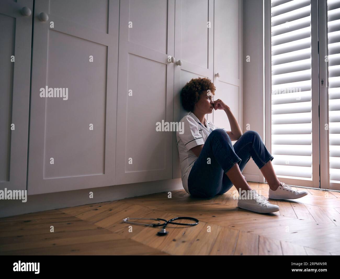 Demotivierte Krankenschwester Trägt Uniform, Die Nach Langer Schicht Zu Hause Auf Dem Boden Sitzt Stockfoto