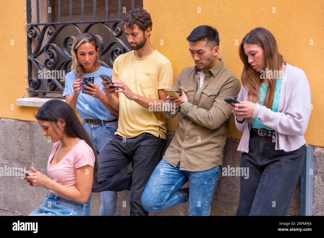 Eine Gruppe von Freunden aus verschiedenen ethnischen Gruppen, die ernsthaft auf das Telefon in der Stadt schauen, Konzept der Jugend, die auf dem Handy hängt Stockfoto