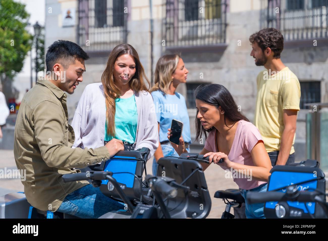 Gruppe von multiethnischen Freunden in der Stadt, die Fahrräder mieten und Spaß mit der Telefon-App haben Stockfoto