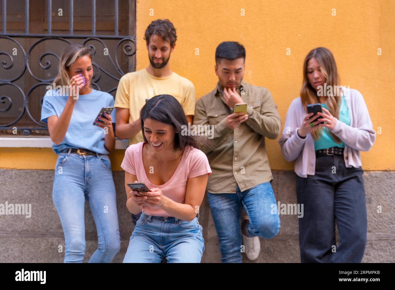 Eine Gruppe von Freunden aus verschiedenen ethnischen Gruppen, die in der Stadt lächelnd auf das Telefon schauen Stockfoto