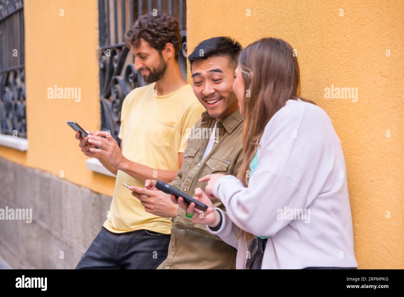 Eine Gruppe von Freunden aus verschiedenen ethnischen Gruppen, die in der Stadt lächelnd auf das Telefon schauen Stockfoto