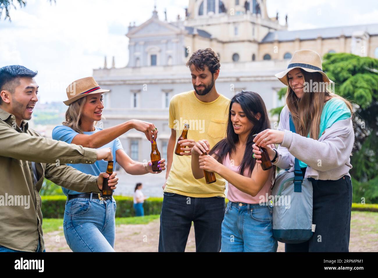 Eine multiethnische Gruppe von Freunden feiert in einem Stadtpark mit Bier. Öffnen der Flaschen Stockfoto