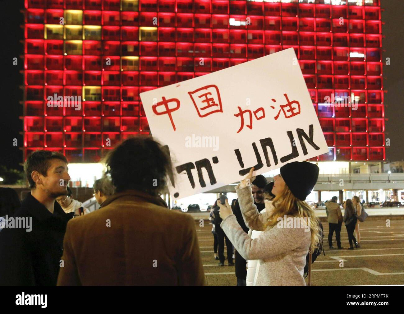 200217 -- PEKING, 17. Februar 2020 -- Eine Frau hält ein Plakat, um China vor der Tel Aviv Municipality Hall zu unterstützen, die mit den Farben der chinesischen Nationalflagge beleuchtet ist, in Solidarität mit Chinas Kampf gegen die neuartige Coronavirus-Epidemie in Tel Aviv, Israel, 11. Februar 2020. ZU XINHUA-SCHLAGZEILEN VON FEB. 17, 2020. Foto von Gil Cohen Magen/Xinhua CHINA-CORONAVIRUS-LÄNDER WELTWEIT UNTERSTÜTZEN ShangxHao PUBLICATIONxNOTxINxCHN Stockfoto