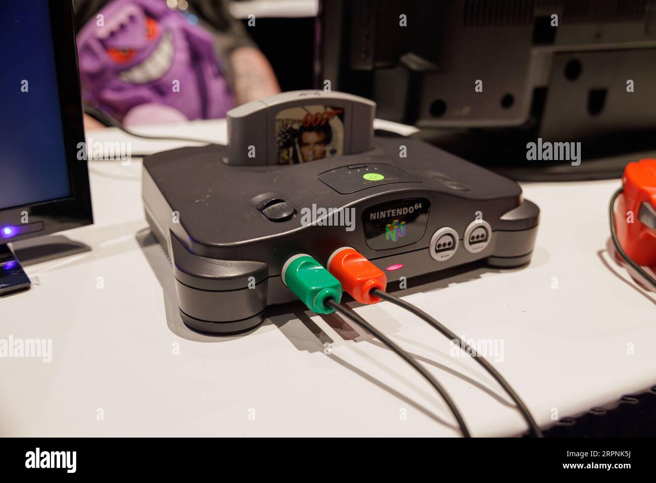 Ein älteres Nintendo 64 Entertainment System ist im Vordergrund des Bildes vor einem modernen Computer mit mehreren Monitoren abgebildet Stockfoto
