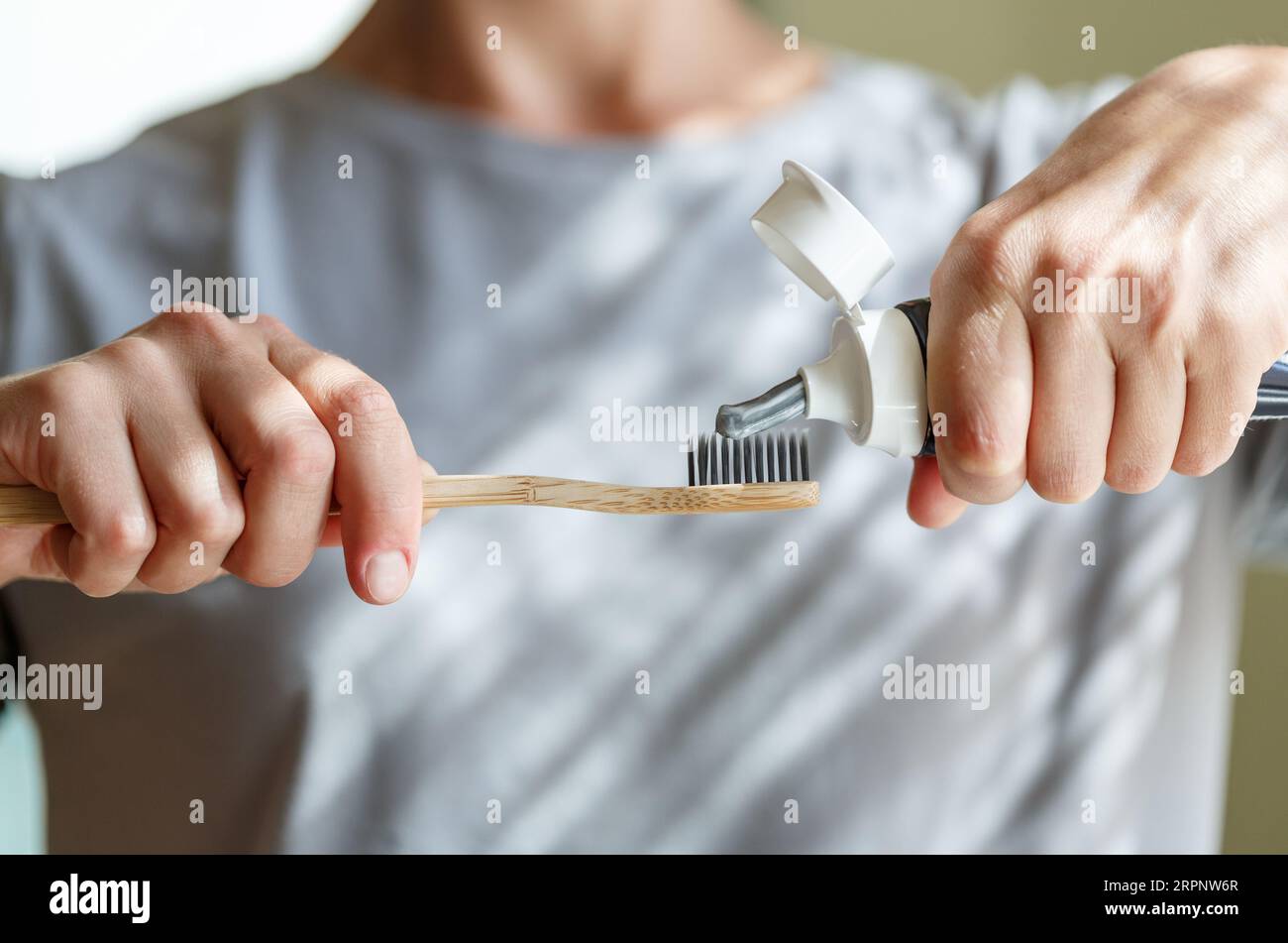 Zahnpasta auf eine Bambuszahnbürste auftragen. Hände, die den Schlauch mit einer Zahnpasta zusammendrücken. Zahnheilkunde und Hygenkonzept. Stockfoto