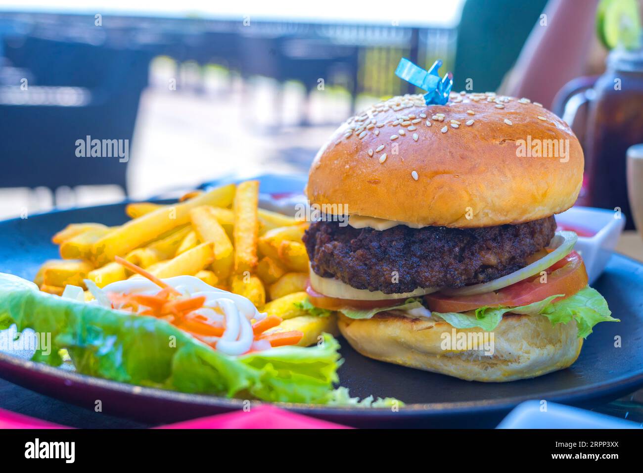 Ein dicker Burger mit Rindfleisch, serviert mit knusprigen Pommes frites, einem Hauch Gemüse, Mayonnaise und Tomatensauce, zusammen mit Chilisauce, auf einem Keramik-Pers Stockfoto