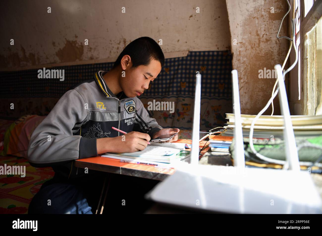 200311 -- ORDOS, 11. März 2020 -- Liu Jincai macht sich Notizen zu Hause, während er dem Onlinekurs seines Englischlehrers im Dorf Hongshuliang von Jungar Banner, Nordchinas Autonome Region Innere Mongolei, 10. März 2020, zuhört. In einer warmen, traditionellen Höhlenwohnung stellt Liu Jincai, ein Schüler der Mittelstufe, einen Klapptisch auf und lernt über ein Mobiltelefon mit WLAN. Mein Sohn musste vor Tagen auf den Gipfel des Berges klettern, um besseres WLAN für den Onlinekurs zu erwerben. Das war unbequem. Lius Mutter Li Yulian sagte: Die Familie lebt am Rande des Loess Plateau, wo die Wi-Fi-Qualität war Stockfoto