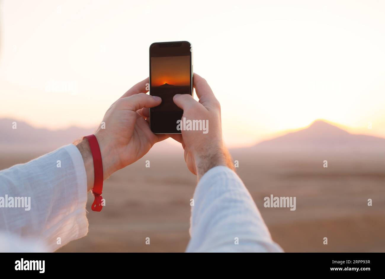 Männliche Hände halten das Handy mit einem Bild des Sonnenuntergangs oder Sonnenaufgangs auf dem Bildschirm Stockfoto