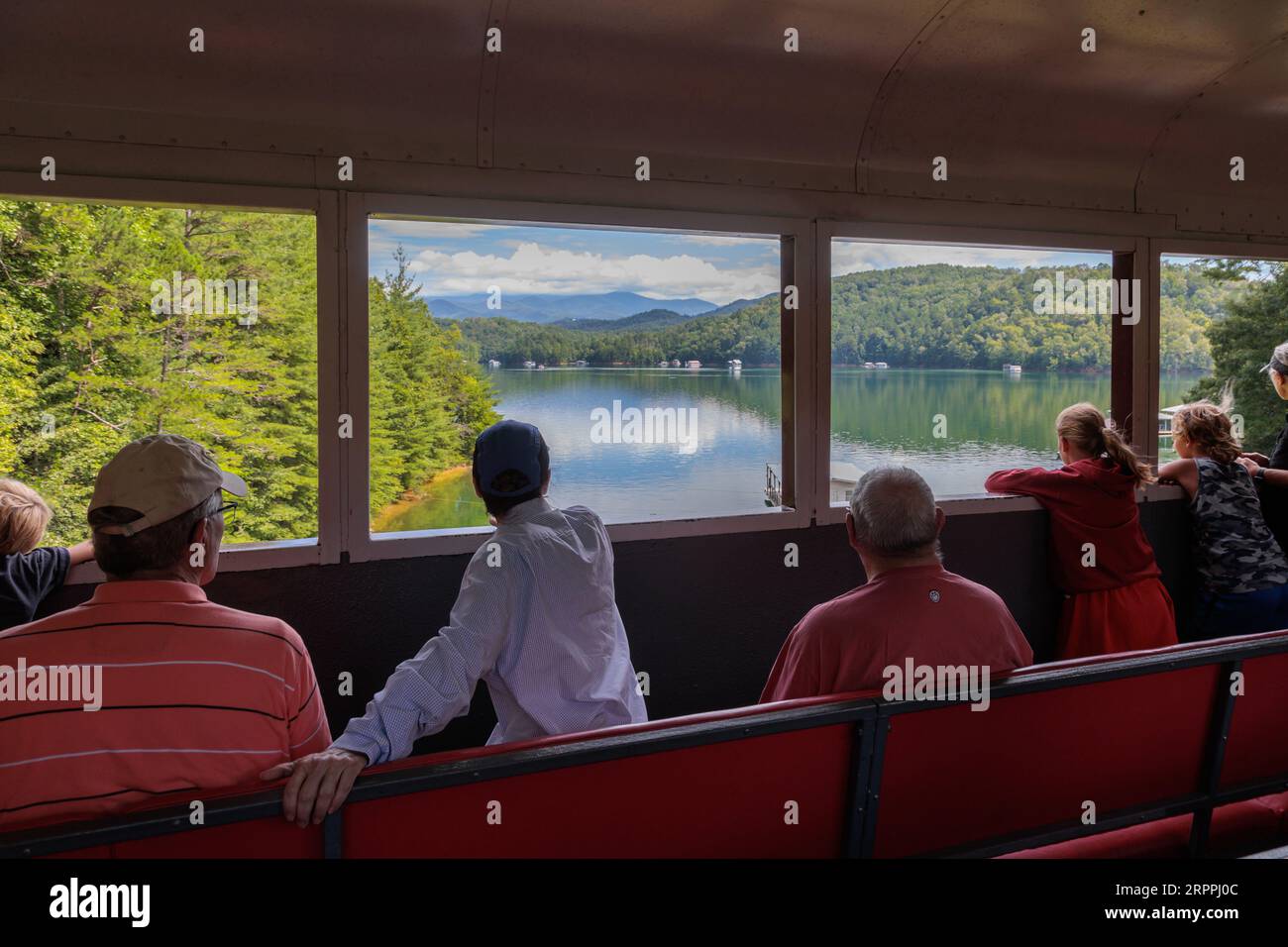 Passagiere der Great Smoky Mountains Railroad blicken auf die Fenster des offenen Zugwagens während eines Ausflugs von Bryson City, North Carolina Stockfoto