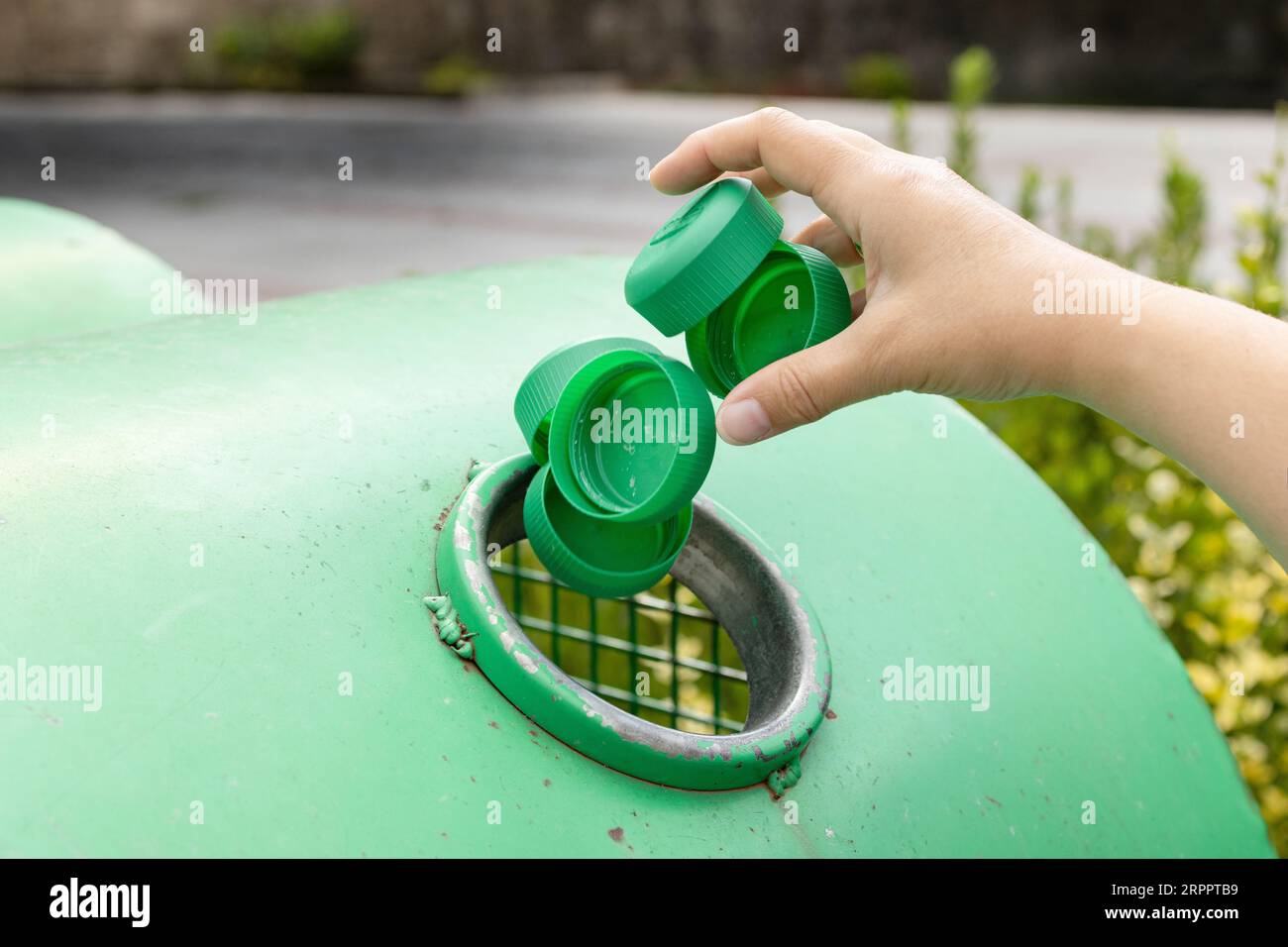 Nahaufnahme einer Hand, die Kunststoffkappen in einen städtischen Recyclingbehälter wirft Stockfoto