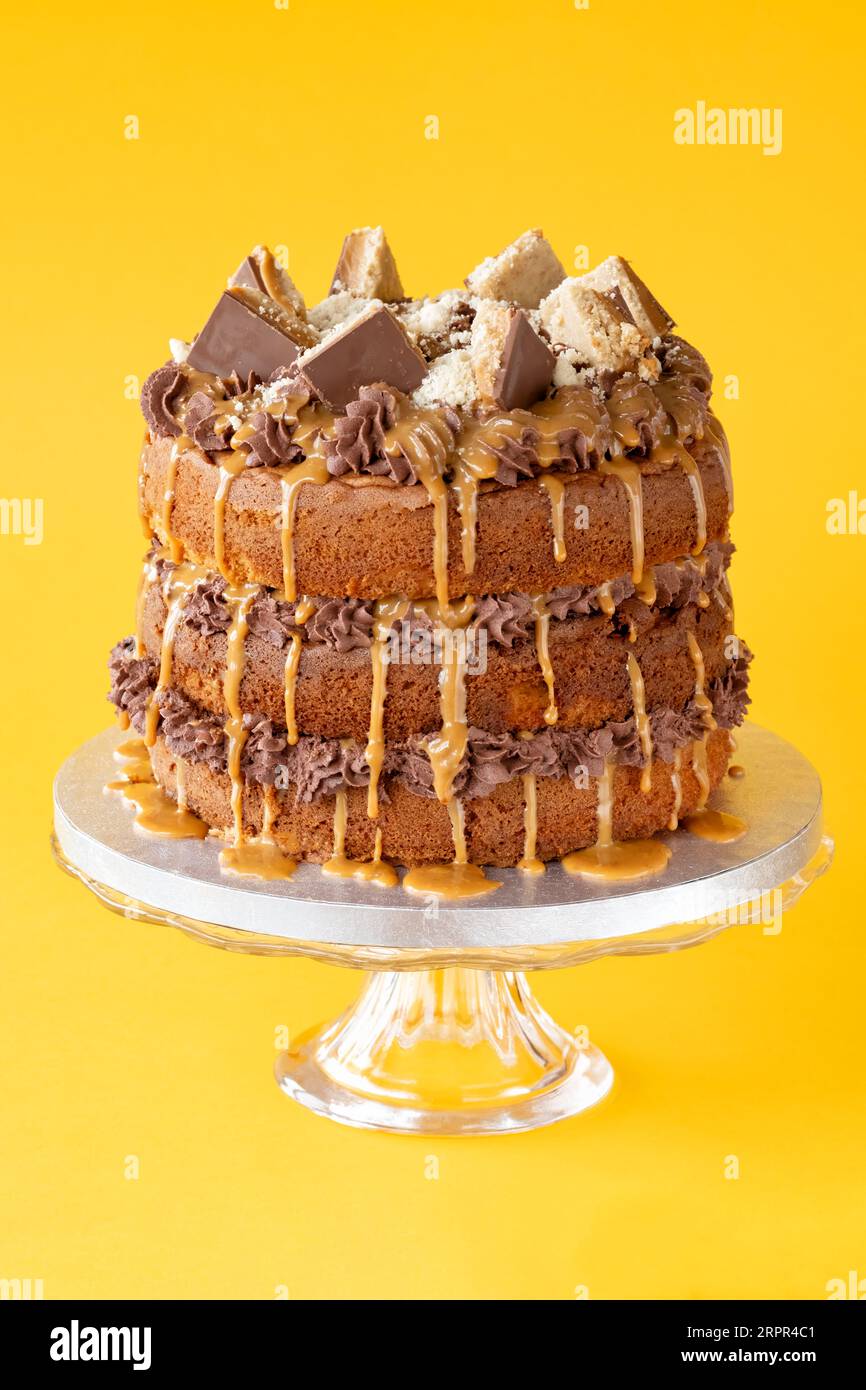 Ein hausgemachter, dreistufiger Millionaires-Kuchen, dekoriert mit Schokoladenbuttercreme, Millionaire-Minibrot und getropftem Karamell Stockfoto