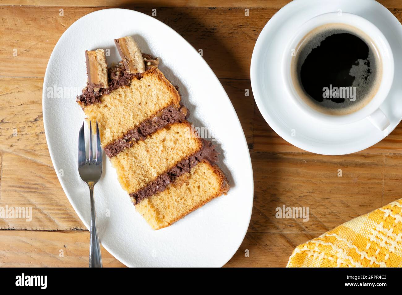 Ein Stück oder eine Portion frisch zubereiteter Millionäre-Biskuitkuchen, serviert auf einem Teller mit einer Konditorgabel und einer frischen Tasse schwarzen Kaffee. Stockfoto