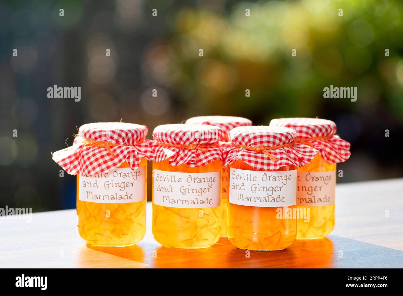 Eine Gruppe von Gläsern mit hausgemachter Sevilla Orange und Ingwermarmelade. Die Gläser haben handgeschriebene Etiketten und Stoffaufsätze über den Deckeln Stockfoto