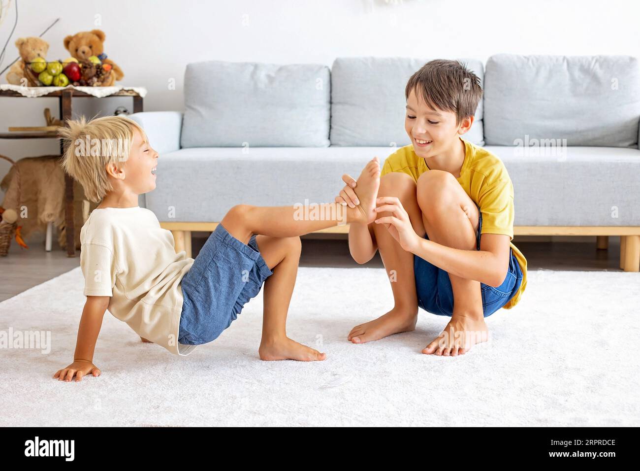 Glückliche positive Kinder, kitzeln auf den Füßen, haben Spaß zusammen, Junge Brüder zu Hause haben einen wunderbaren Tag der Freude zusammen Stockfoto