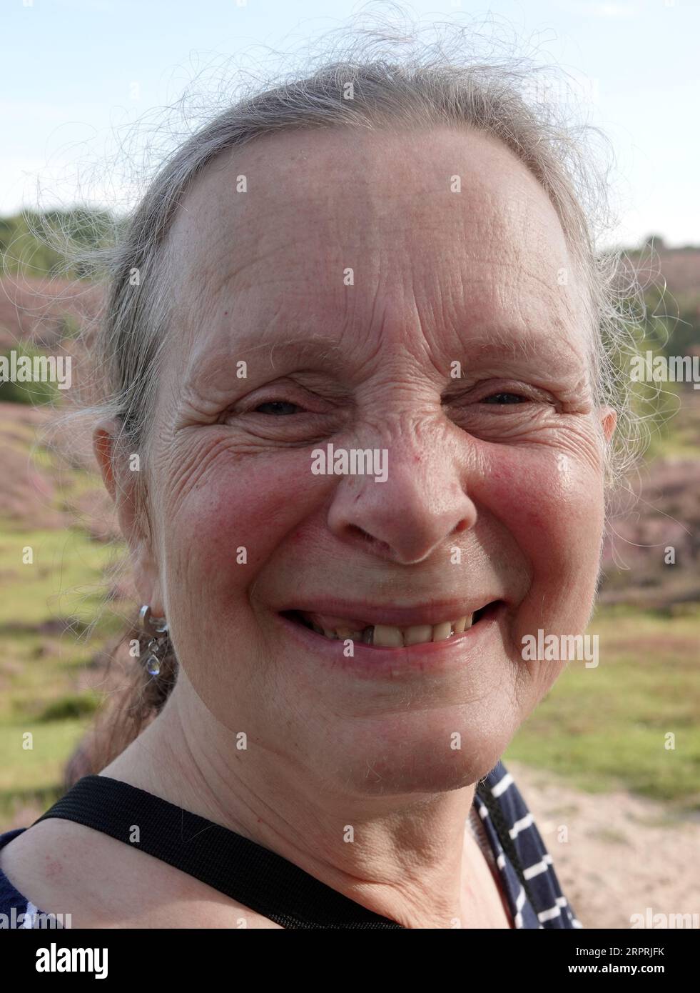 Frau in ihren Sechzigern ohne Make-up sieht glücklich in die Kamera. Eines ihrer Zähne versagt Stockfoto