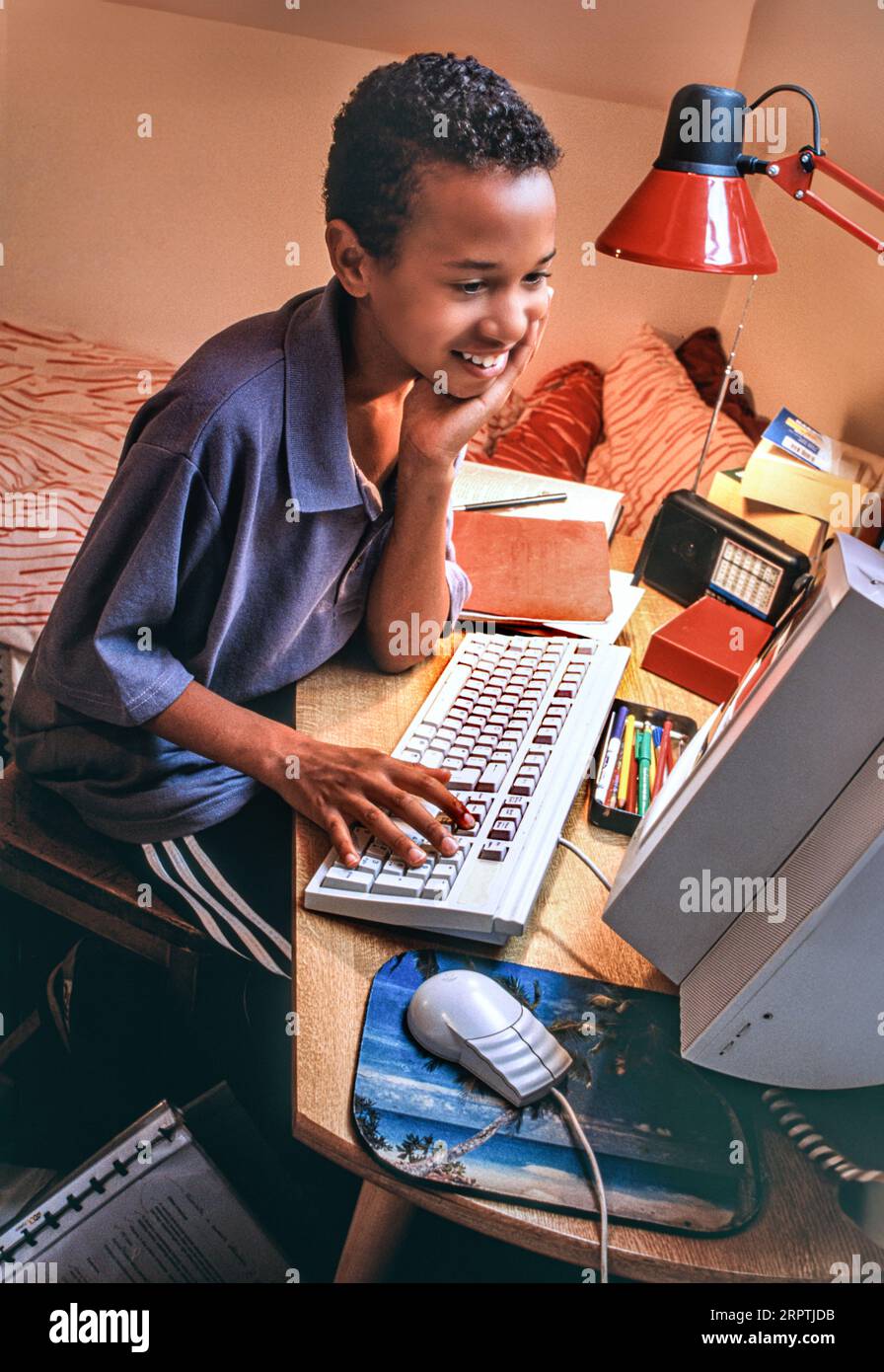 1990er Jahre Home Computer Boy 7-9 Jahre erster Computer Mode Stil 1990er Jahre Surfzimmer Afrikanischer Karibischer Junge in seinem Schlafzimmer glücklich entspanntes Surfen Spielen Lernen auf seinem ersten Computer 1995 Ära Stockfoto