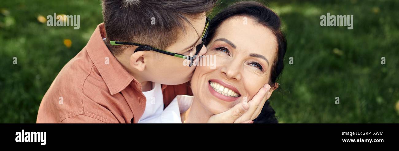 Kind mit Down-Syndrom, in Brille, fröhliche Mutter im Park küssen, emotionale Verbindung, Banner Stockfoto