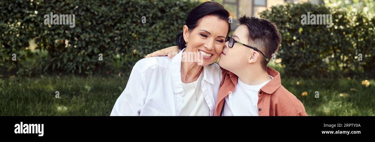 Junge mit Down-Syndrom, der fröhliche Mutter im Park küsst, emotionale Verbindung, Liebe, Banner Stockfoto