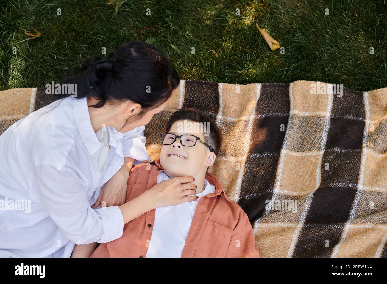 Draufsicht auf Mutter in der Nähe von Happy Son mit Down-Syndrom auf Decke im Park, bedingungslose Liebe Stockfoto