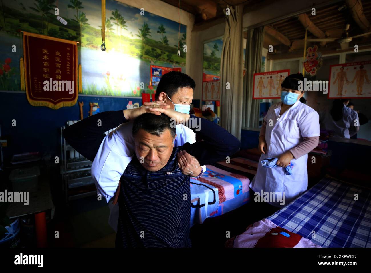 200425 -- LIAOCHENG, 25. April 2020 -- Behinderter Wang Guangjun Back L massiert einen Kunden, während seine ebenfalls behinderte Frau Wang Yujing in ihrem Massagesalon im Shaoyuehe Village im Dongchangfu Bezirk der Stadt Liaocheng, ostchinesische Provinz Shandong, am 22. April 2020 schaut. Wang Guangjun und seine Frau Wang Yujing sind behinderte Menschen, die im Dorf leben. Erstere waren durch linke Armwunden und letztere durch Nervenverletzungen in der Taille behindert. Sie leben in wirtschaftlichen Schwierigkeiten, da sie keine schwere körperliche Arbeit verrichten können. 2015 wurde Wangs Familie als armutsgeschädigter Haushalt identifiziert Stockfoto