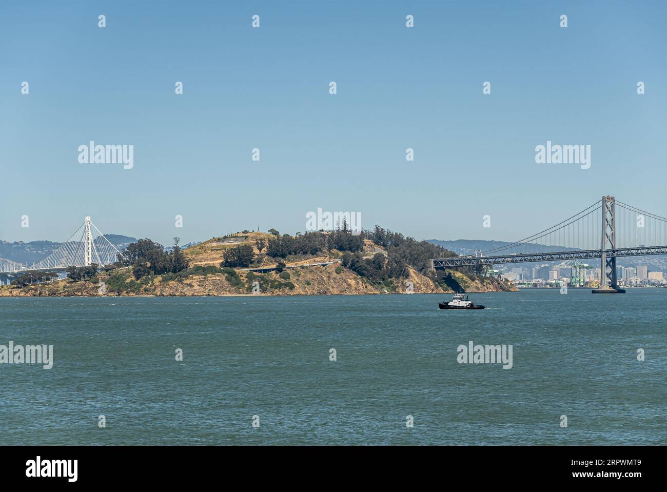 San Francisco, CA, USA - 13. Juli 2023: Yerba Buena Island und SF-Oakland Bay Bridge auf beiden Seiten unter blauem Himmel und kleines Boot auf blaugrünem Wasser Stockfoto