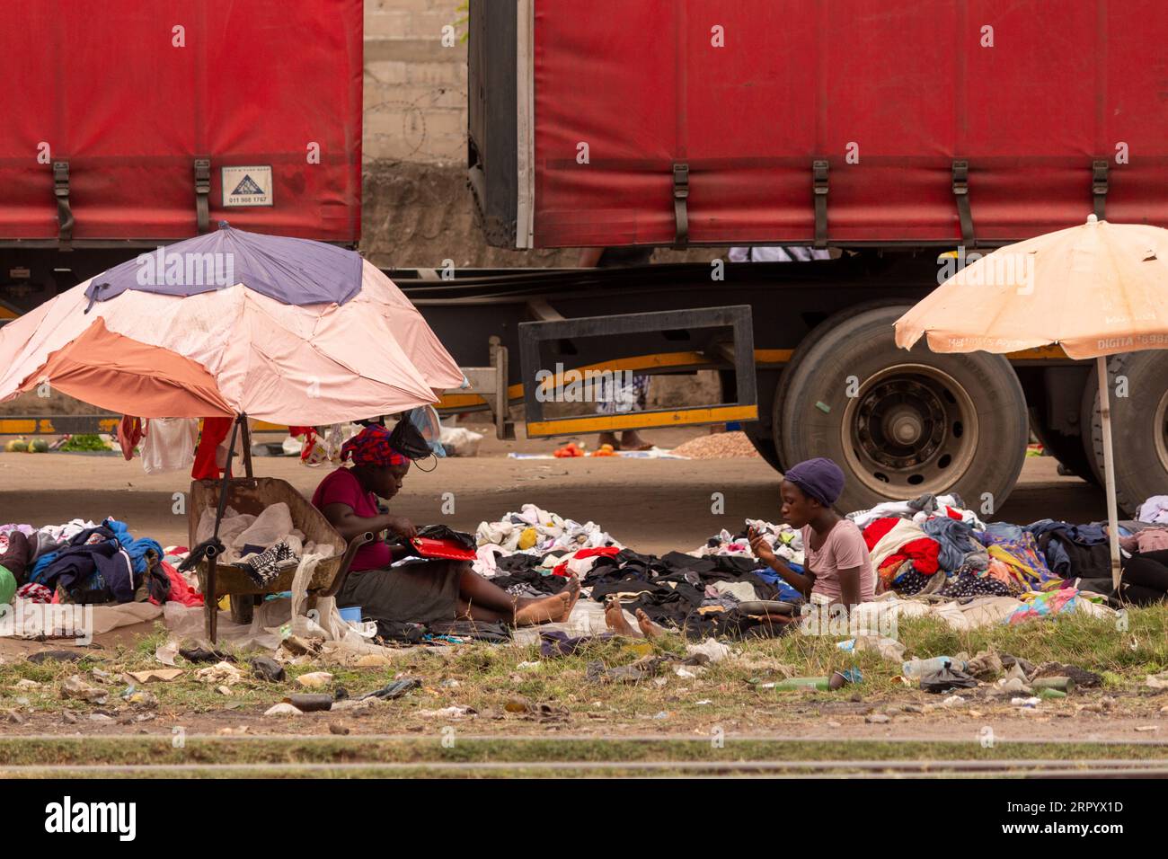 Frauen, die eine Mittagspause machen, während sie gebrauchte Kleidung an einem geschäftigen Straßenrand verkaufen Stockfoto