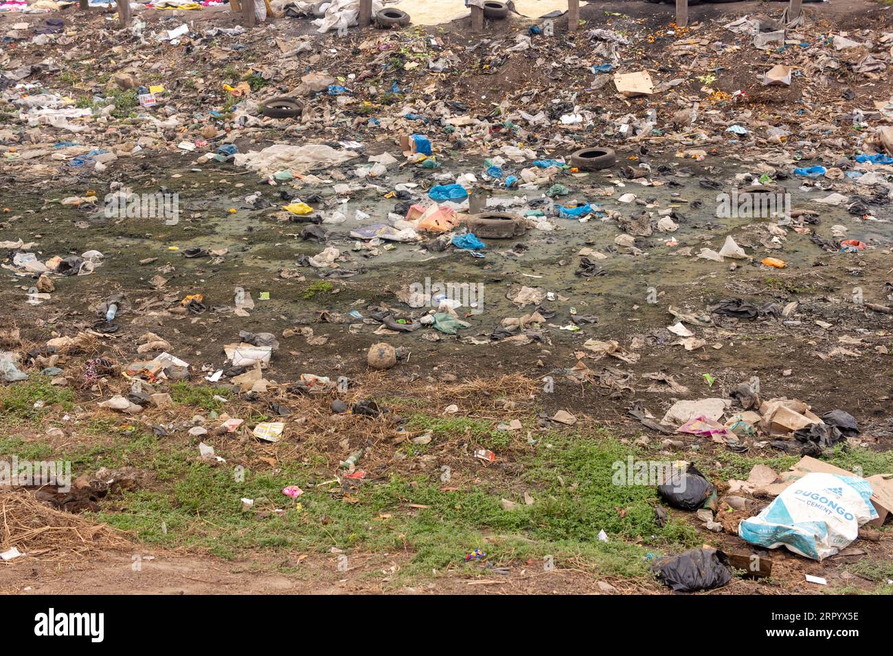 Waste-filled Valley in der Nähe der Main Road mit weggeworfenen Kunststoffverpackungen, stehendem Wasser und alten Reifen Stockfoto