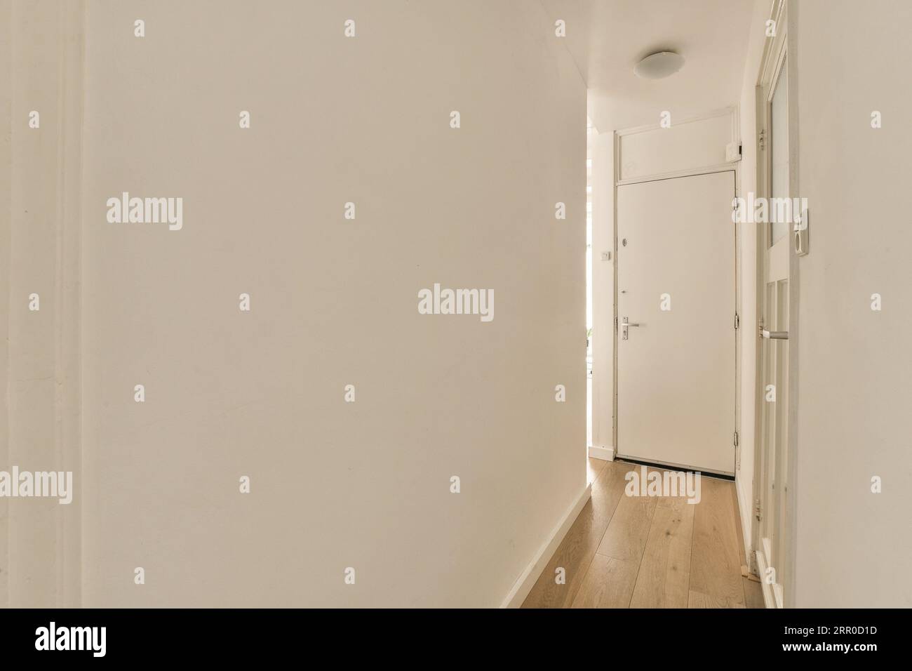 Ein leerer Raum mit weißen Wänden und Holzfußboden auf der linken Seite des Zimmers, es gibt eine Tür auf der rechten Seite Stockfoto