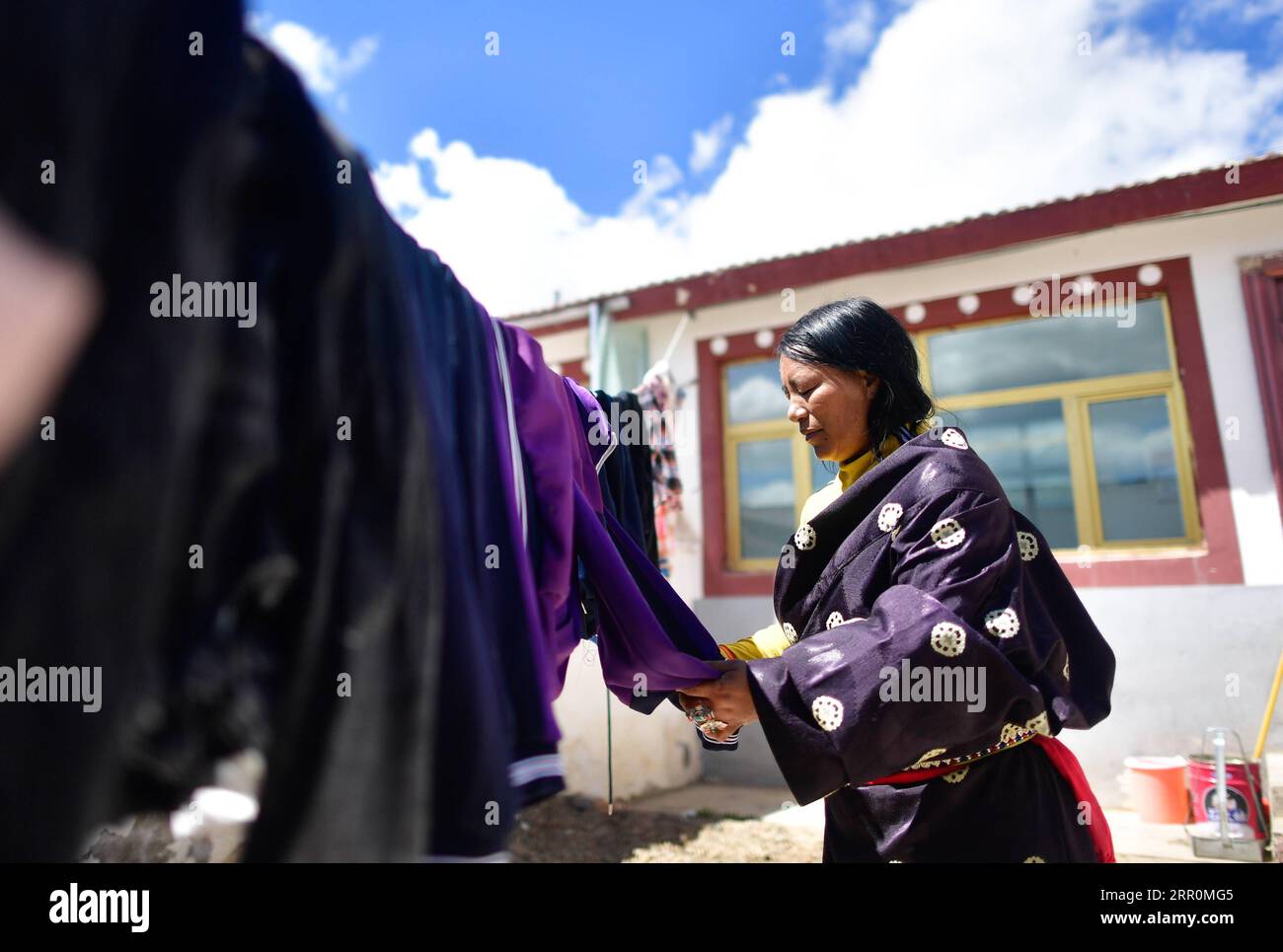 200820 -- GOLOG, 20. August 2020 -- Villager Degyi trocknet Kleidung in ihrem Innenhof im Dorf Ghadan in der Gemeinde Machali, County Madoi, Golog Tibetan Autonomous Prefecture, nordwestchinesische Provinz Qinghai, 19. August 2020. Im Oktober 2018 sind insgesamt 1.036 registrierte, von Armut betroffene Einwohner von den weniger gastfreundlichen Ländern des Madoi County nach Ghadan gezogen, einem neu errichteten Umsiedlungsdorf im Quellgebiet des Gelben Flusses. Das neue Dorf verfügt über bessere Transportmöglichkeiten, was es den Dorfbewohnern erleichtert, in anderen Städten Arbeitsplätze zu finden oder Unternehmen zu gründen. Inzwischen werden viele Dorfbewohner als Envir bezahlt Stockfoto